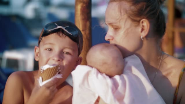 Mother-with-baby-and-elder-son-at-the-beach.-Boy-eating-ice-cream