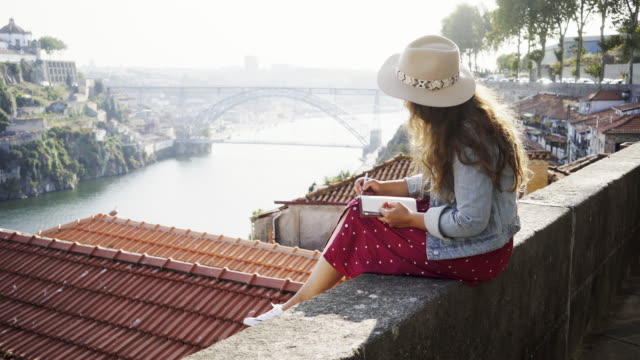Young-lady-with-notebook-and-pen-sitting-near-roofs
