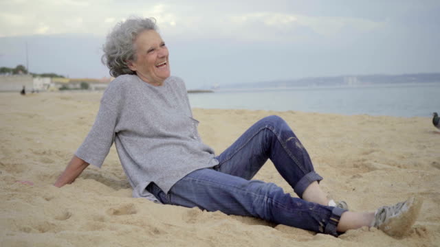 Schöne-ältere-Frau-auf-Sand-sitzen-und-lachen.