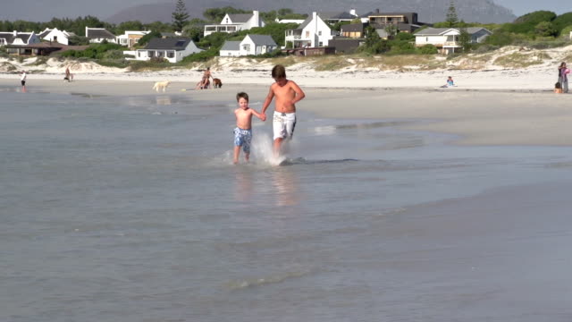 Dos-chicos-corriendo-hacia-la-cámara-en-la-playa,-de-Cape-Town