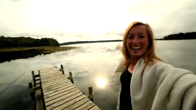 Young-woman-on-wooden-wharf-above-lake,-takes-selfie-portrait
