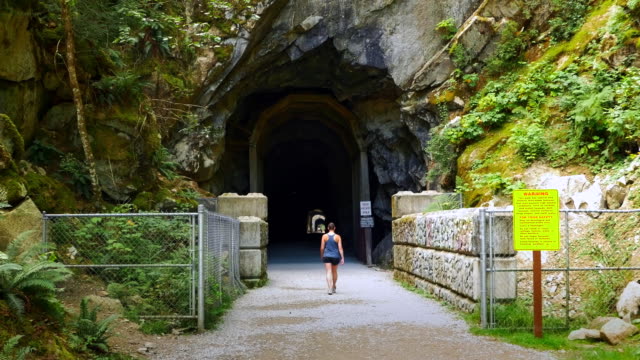 Mujer-entra-en-el-túnel-del-tren,-camino-de-ripio,-túneles-de-Othello,-esperanza-BC-Canadá