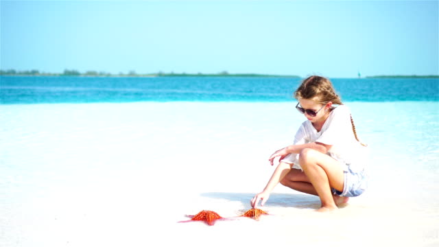 Entzückende-kleine-Mädchen-mit-riesigen-roten-Seestern-auf-weißen-leeren-Strand