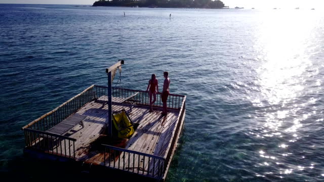 v03831-fliegenden-Drohne-Luftaufnahme-der-Malediven-weißen-Sandstrand-2-Personen-junges-Paar-Mann-Frau-entspannend-auf-sonnigen-tropischen-Inselparadies-mit-Aqua-blau-Himmel-Meer-Wasser-Ozean-4k-schwimmenden-Ponton-Steg-Sonnenbaden-zusammen