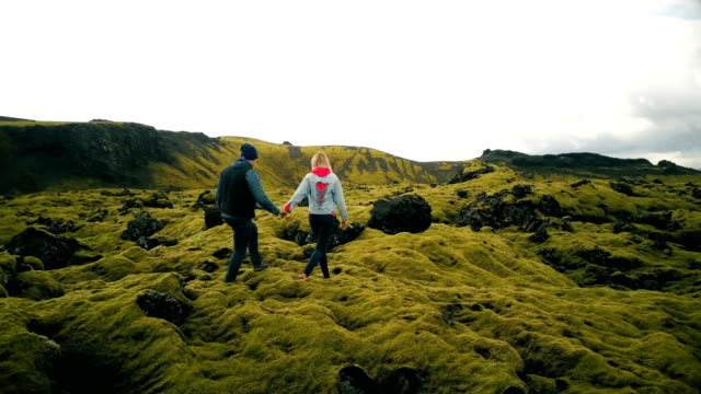Aerial-view-of-couple-walking-through-the-lava-fields-in-iceland.-Man-and-woman-sit-on-the-rock,-enjoying-the-landscape
