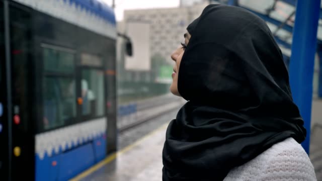 Young-muslim-woman-in-hijab-is-watching-how-train-is-coming,-raining,-religion-concept,-urban-concept