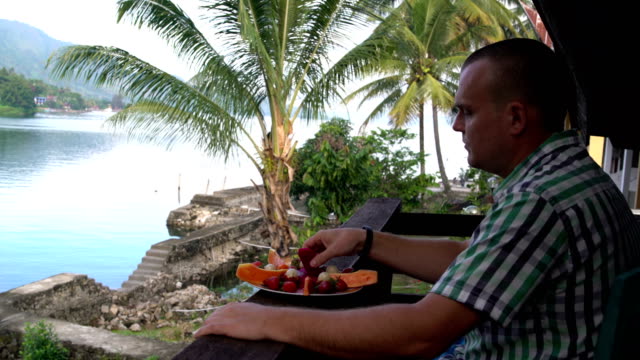 Ein-Mann-isst-eine-Pitahaya-Frucht-und-schaut-auf-den-See-und-die-Berge