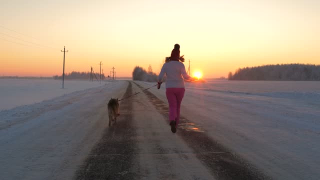 Frau-läuft-mit-einem-Hund-an-einem-Winterabend-auf-dem-Weg-zu-den-scharlachroten-Sonnenuntergang-treffen