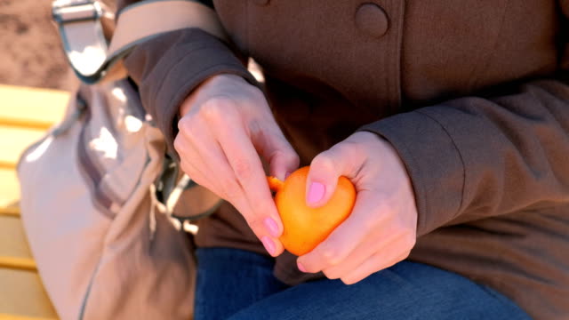 Close-up-woman's-hands-peels-tangerine-in-park.