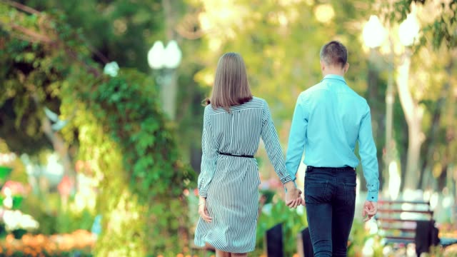 Young-couple-walk-through-a-city-park-together-heading-away-from-the-camera