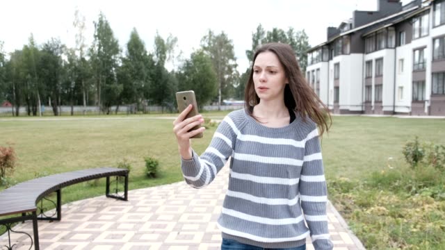 Beautiful-brunette-woman-blogger-talk-a-video-chat-on-mobile-phone-walking-near-the-home.
