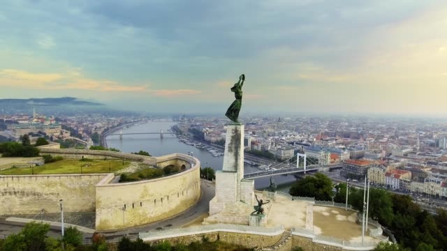 Flying-around-of-Statue-of-Liberty-with-the-skyline-of-Budapest-at-background.-Budapest,-Hungary---4K-aerial-footage-at-sunrise