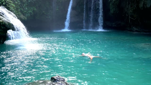 Young-woman-swimming-in-idyllic-waterfall-in-tropical-forest-located-in-the-Philippines-Islands.-People-travel-fun-enjoyment-vacations-concept
