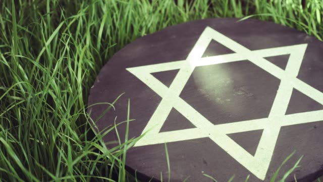 White-Star-of-David-on-a-black-stone-round-on-a-grass-background,-rotation-360-degrees.