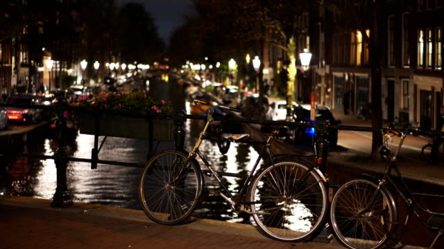 eine-Nachtaufnahme-von-einem-Fahrrad-angekettet-an-einer-Brücke-über-einen-Kanal-in-amsterdam