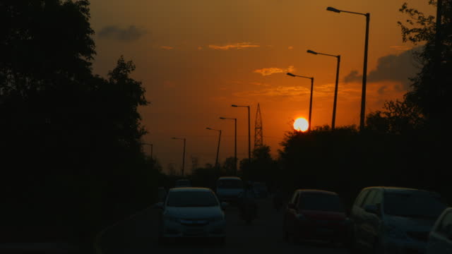 Locked-on-shot-of-traffic-moving-on-road-at-sunset,-Delhi,-India