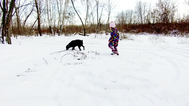 Kleines-Mädchen-spielt-mit-ihren-schwarzen-Labrador-auf-Schnee