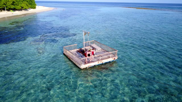 v03852-vuelo-drone-vista-aérea-de-Maldivas-playa-2-personas-pareja-hombre-mujer-relajante-en-la-isla-de-paraíso-tropical-soleado-con-cielo-azul-aqua-agua-mar-4k-flotante-pontoon-embarcadero-el-sol-juntos