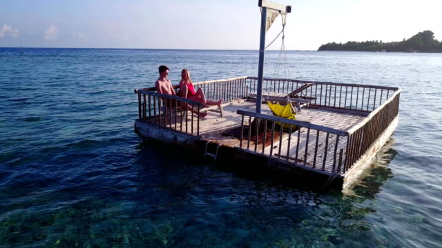 v03847-fliegenden-Drohne-Luftaufnahme-der-Malediven-weißen-Sandstrand-2-Personen-junges-Paar-Mann-Frau-entspannend-auf-sonnigen-tropischen-Inselparadies-mit-Aqua-blau-Himmel-Meer-Wasser-Ozean-4k-schwimmenden-Ponton-Steg-Sonnenbaden-zusammen