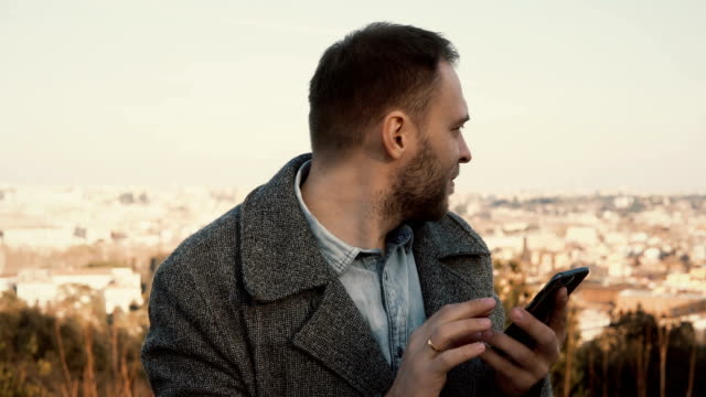 Porträt-von-schönen-jungen-Mann-stehend-auf-das-Panorama-von-Rom,-Italien.-Männlich-verwenden-Sie-das-Smartphone-außerhalb