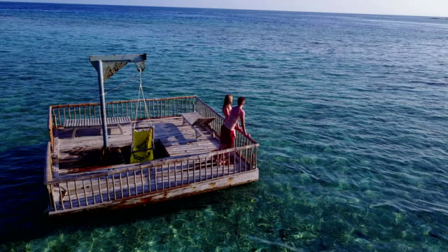 v03856-vuelo-drone-vista-aérea-de-Maldivas-playa-2-personas-pareja-hombre-mujer-relajante-en-la-isla-de-paraíso-tropical-soleado-con-cielo-azul-aqua-agua-mar-4k-flotante-pontoon-embarcadero-el-sol-juntos