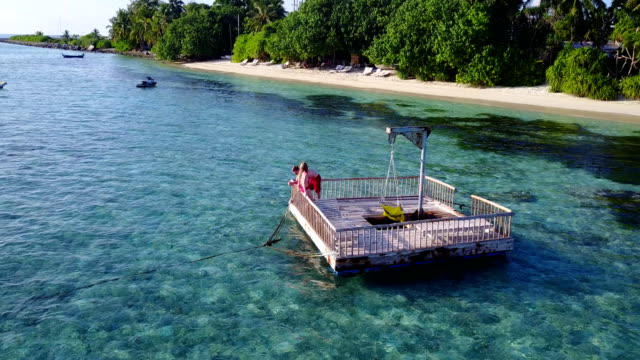 v03853-fliegenden-Drohne-Luftaufnahme-der-Malediven-weißen-Sandstrand-2-Personen-junges-Paar-Mann-Frau-entspannend-auf-sonnigen-tropischen-Inselparadies-mit-Aqua-blau-Himmel-Meer-Wasser-Ozean-4k-schwimmenden-Ponton-Steg-Sonnenbaden-zusammen