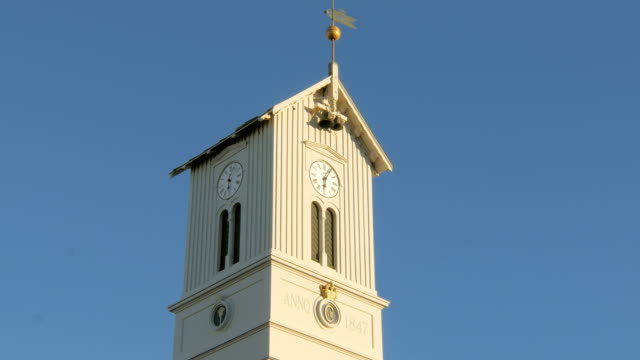 top-of-tower-of-icelandic-church-with-clock,-bells-and-weathercock,-against-clear-blue-sky