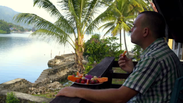 Ein-Mann-isst-Papaya-und-schaut-auf-den-See-und-die-Berge