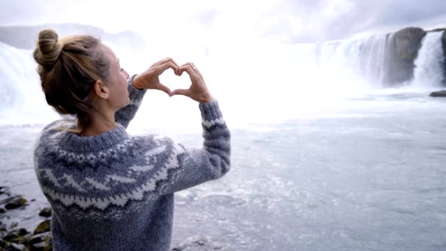 Mujer-joven-en-Islandia-que-marco-del-dedo-corazón-forma-en-espectacular-cascada