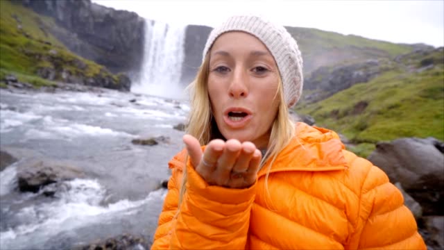 Joven-tomando-selfie-retrato-con-magnífica-cascada-en-Islandia,-que-sopla-un-beso-a-la-cámara.-Gente-viaje-exploración-concepto