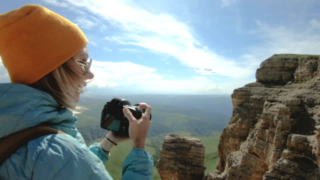 Fotógrafo-de-chica-rubia-de-la-tapa-tiene-una-foto-en-su-cámara-digital-con-un-fondo-de-rocas-en-el-Cáucaso