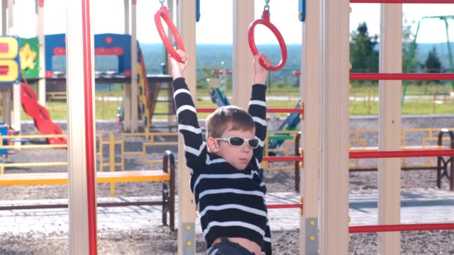 Sieben-Jahr-Alter-Junge-hängt-an-der-Gymnastik-Ringen-auf-dem-Spielplatz.