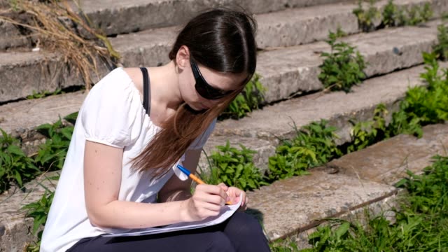 Young-girl-making-her-tasks-and-homework-sitting-in-park.-College-student.