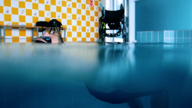 Hombre-discapacitado-sobre-el-agua-en-la-espalda-en-una-piscina.-Tiro-bajo-el-agua