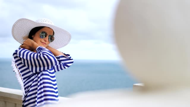 Mujer-elegante-de-la-vista-lateral-con-sombrero-y-gafas-de-sol-admirando-el-mar-y-el-cielo-en-el-balcón-o-terraza
