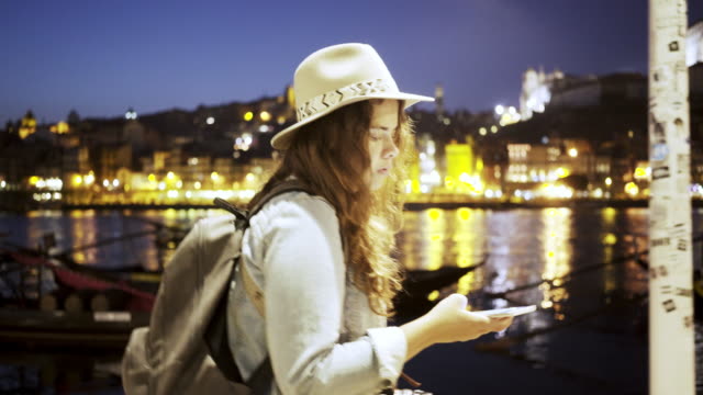 Lady-in-hat-with-backpack-and-smartphone-on-embankment
