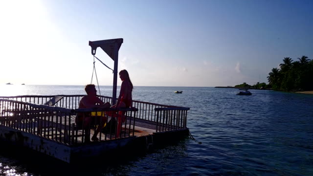 v03830-vuelo-drone-vista-aérea-de-Maldivas-playa-2-personas-pareja-hombre-mujer-relajante-en-la-isla-de-paraíso-tropical-soleado-con-cielo-azul-aqua-agua-mar-4k-flotante-pontoon-embarcadero-el-sol-juntos