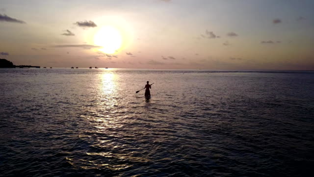 v04102-fliegenden-Drohne-Luftaufnahme-der-Malediven-weißen-Sandstrand-2-Personen-junges-Paar-Mann-Frau-Paddleboard-Rudern-Sonnenuntergang-Sonnenaufgang-auf-sonnigen-tropischen-Inselparadies-mit-Aqua-blau-Himmel-Meer-Wasser-Ozean-4k