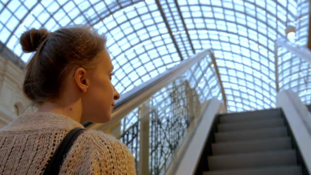 Mujer-joven-en-escalera-mecánica-en-movimiento-y-mirando-a-su-alrededor-en-el-centro-comercial