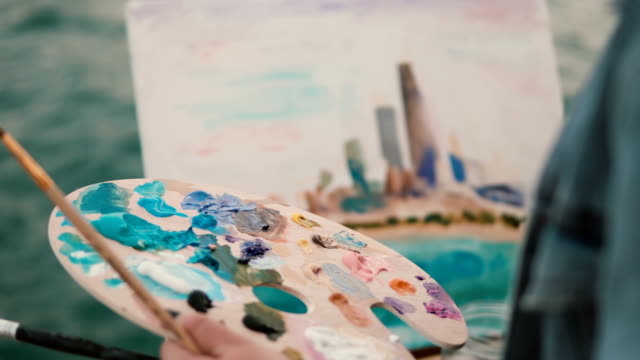 Closeup-view-of-female-hand-with-brush-and-palette-painting-the-picture-on-the-shore-of-Michigan-lake,-Chicago,-America
