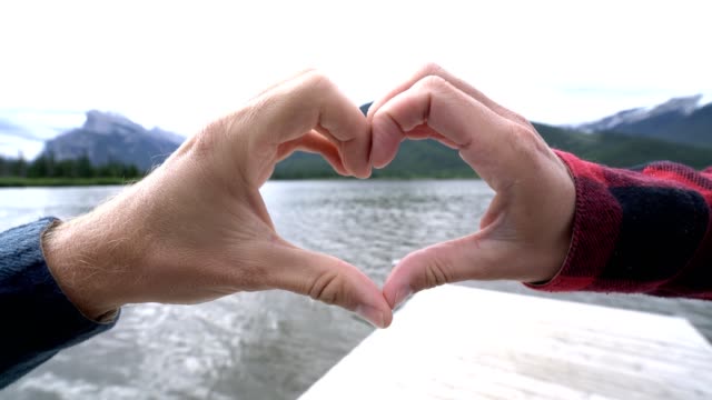 Close-up-on-hands-making-heart-shape-frame-on-mountain-lake-landscape