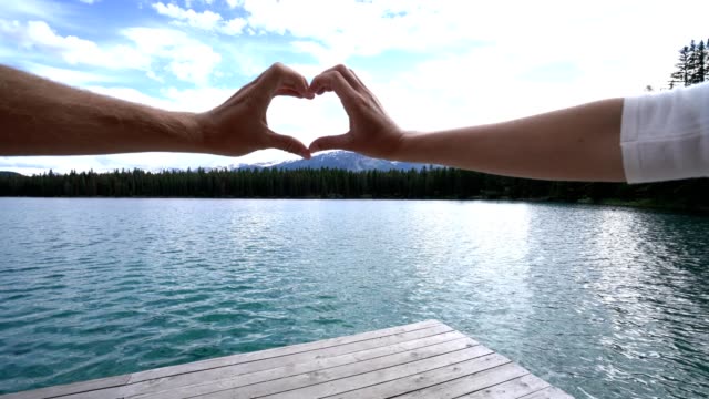 Close-up-on-hands-making-heart-shape-frame-on-mountain-lake-landscape