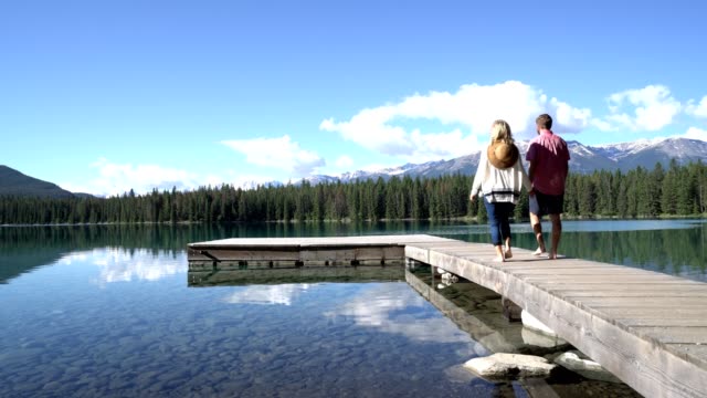 Joven-pareja-dando-un-paseo-largo-muelle-de-madera-sobre-el-impresionante-paisaje-de-lago-de-montaña