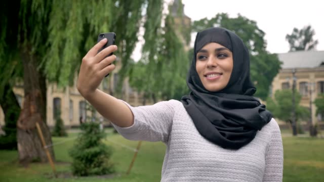Young-beautiful-muslim-woman-in-hijab-is-making-selfie-on-smartphone-in-blue-weather,-communication-concept,-religious-concept