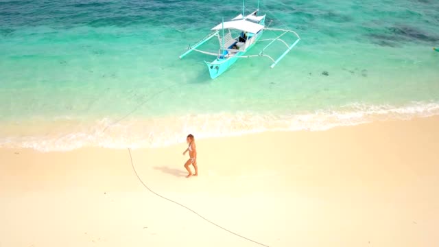 Drone-shot-aerial-view-of-young-woman-walking-on-idyllic-tropical-beach