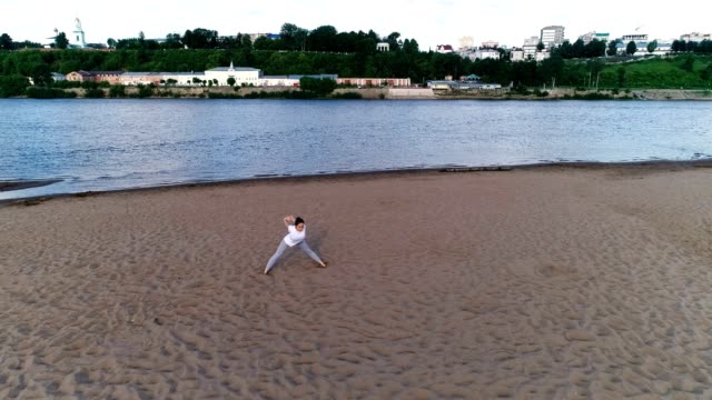 Mujer-haciendo-yoga-en-la-playa-por-el-río-en-la-ciudad.-Hermosa-vista.