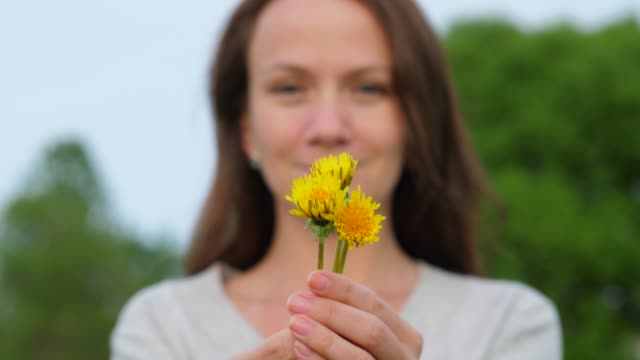 Young-woman-hold-in-hands-small-bunch-of-dandelion-flowers