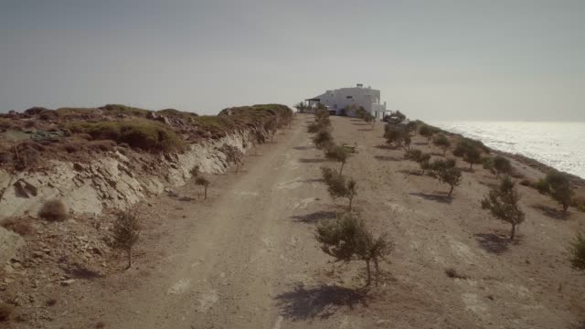 Vista-aérea-de-una-carretera-de-tierra-con-una-casa-grande-en-el-mar,-Grecia.