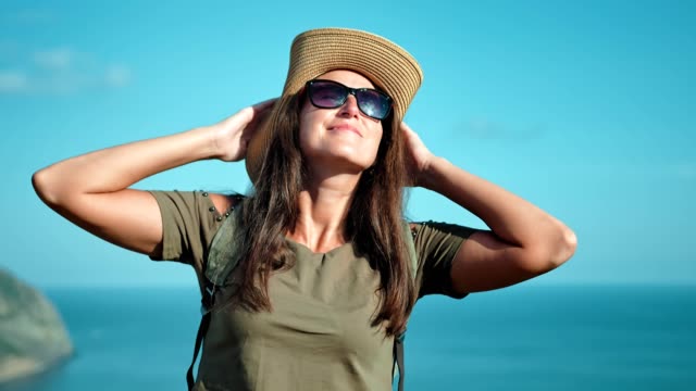 Portrait-of-woman-hiker-in-hat-and-sunglasses-enjoying-sun-raising-hands-getting-big-thumbs-up