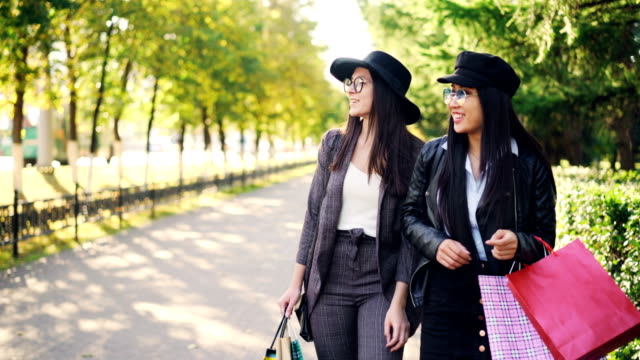 Pretty-girls-friends-are-having-fun-in-the-street-walking-with-shopping-bags,-laughing-and-talking-enjoying-free-time.-Consumerism,-friendship-and-youth-concept.
